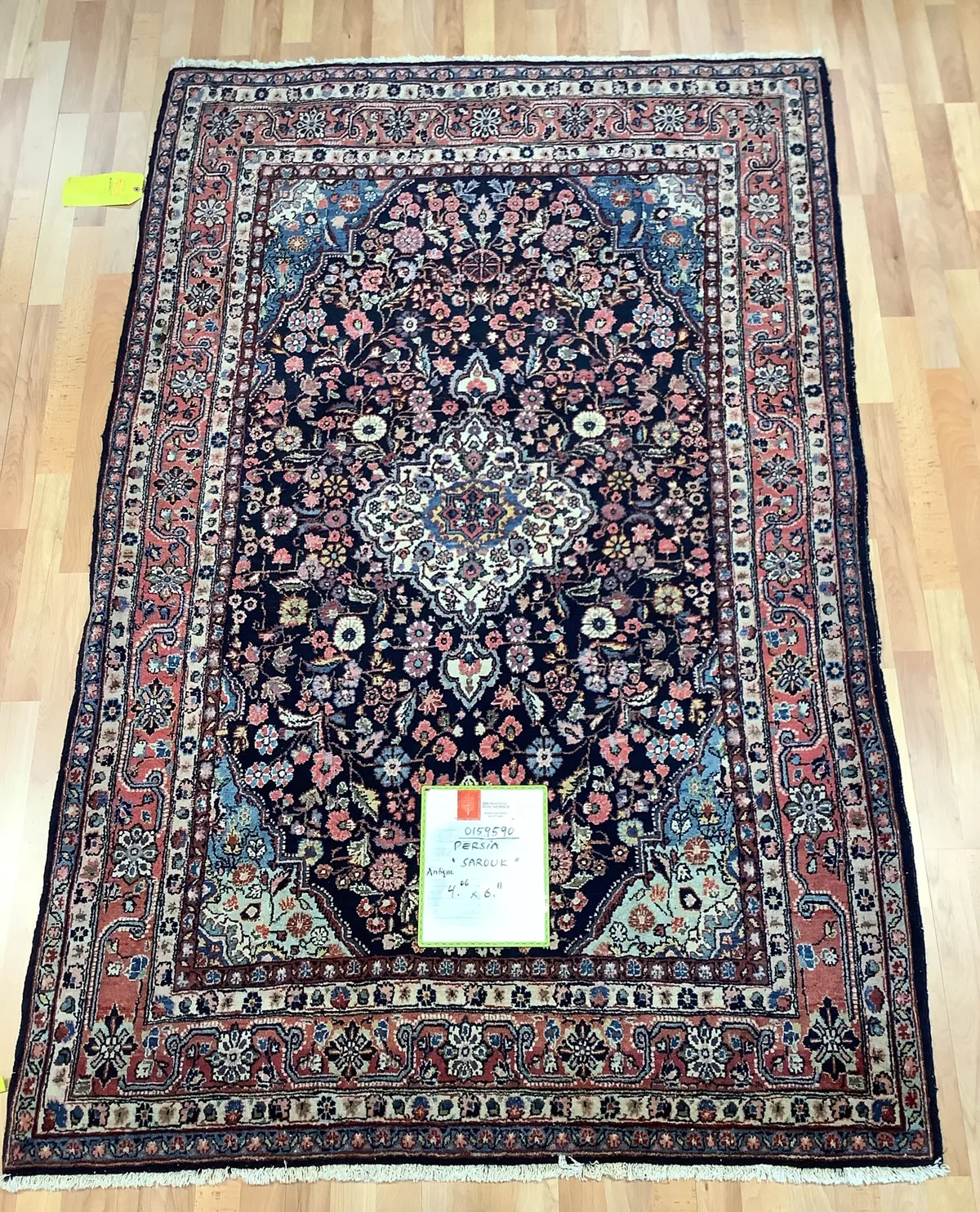 Antique Persian Sarouk rug with a navy field, ivory center medallion, and red floral border, laid flat at Oriental Rug Works in Keene, NH