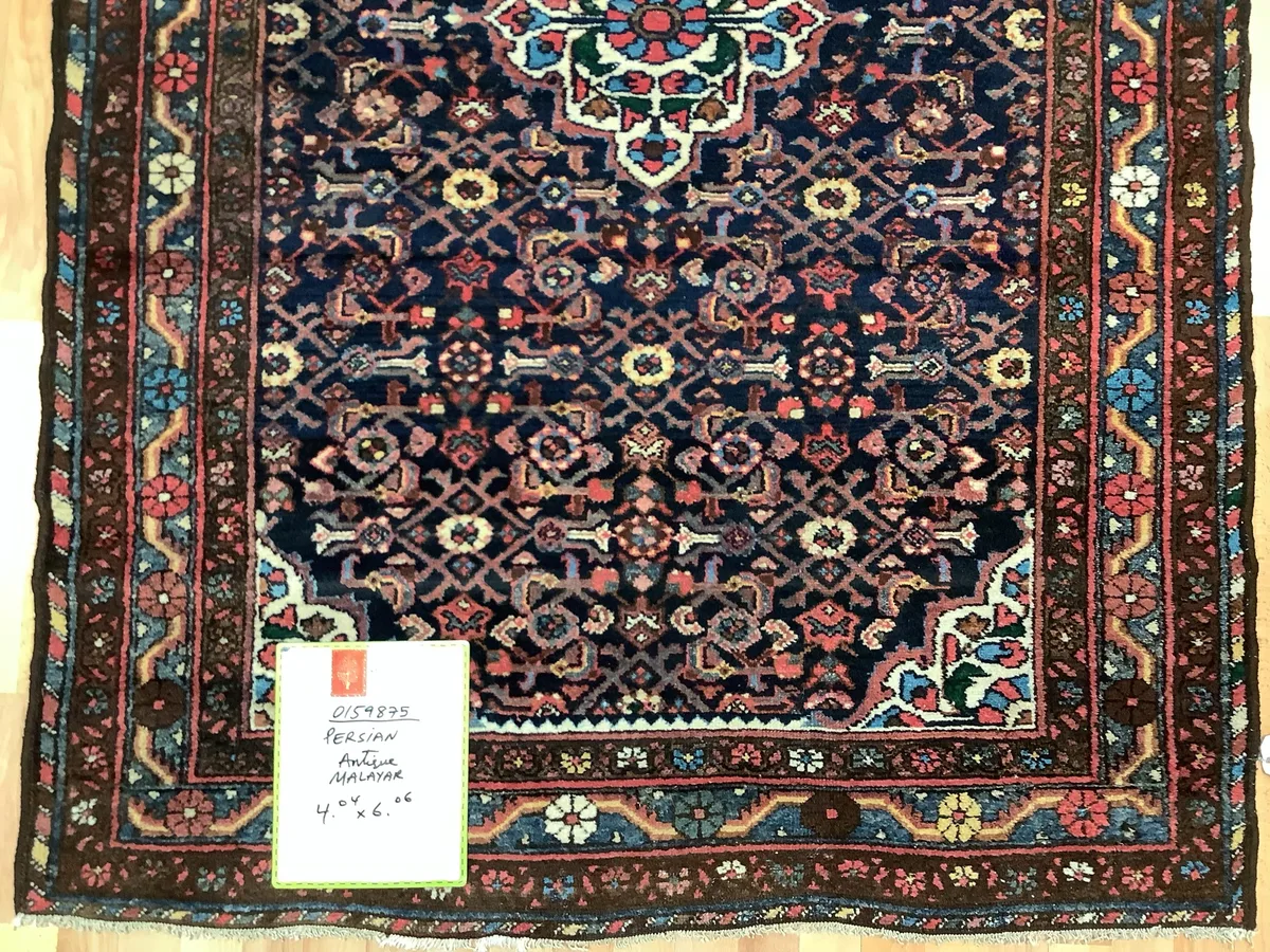 Antique Persian Malayer rug with a dense navy field of small red and ivory flowers, photographed on a wood floor at Oriental Rug Works in Keene, NH