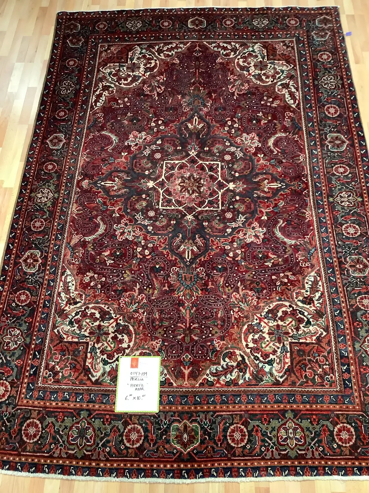 Red Persian Heriz rug with a large ivory and navy center medallion, laid flat on a wood floor at Oriental Rug Works in Keene, NH